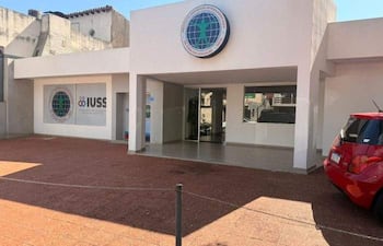 Edificio moderno con fachada blanca y señalización 'IUSS', entrada central y automóvil rojo estacionado a la derecha.