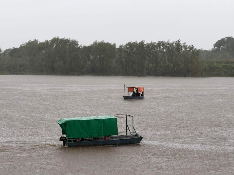 Bote verde y bote naranja en el Río Paraguay, rodeados de árboles, mientras la lluvia agita la superficie del agua.