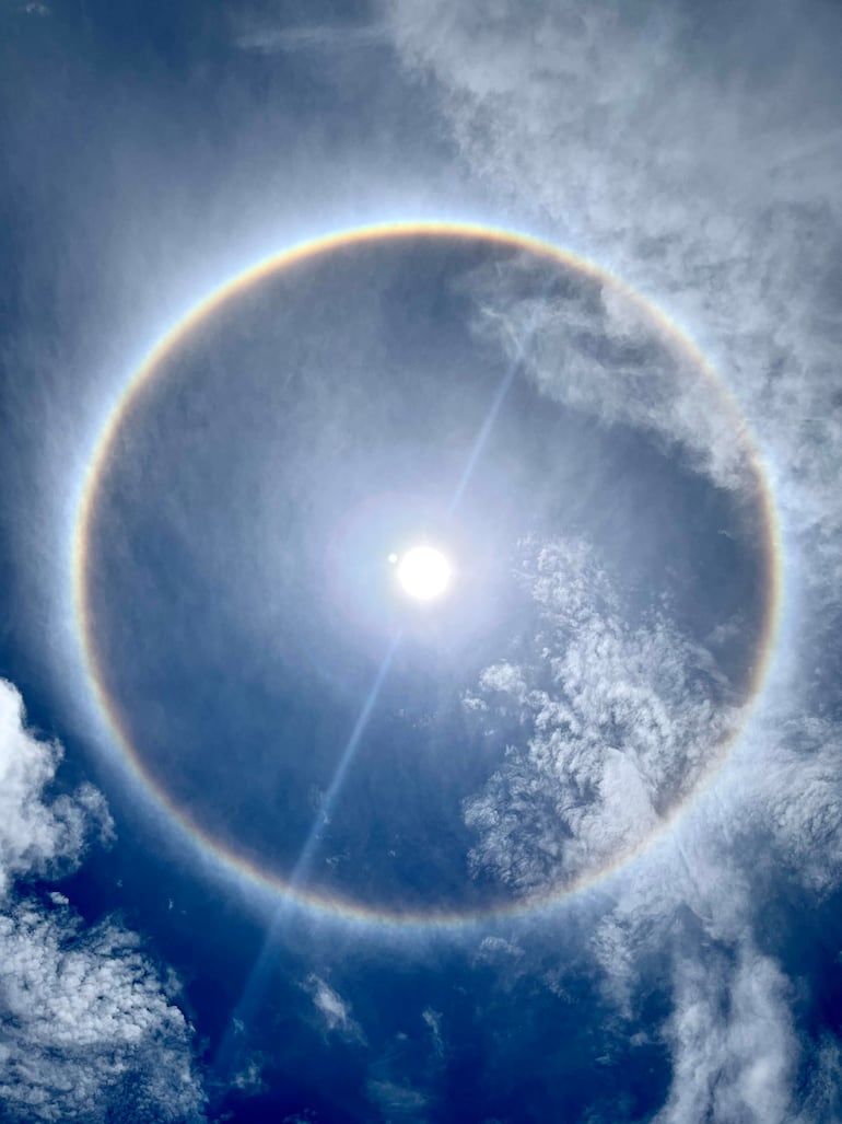 Sol radiante rodeado de un brillante halo en un cielo azul despejado con nubes esponjosas.