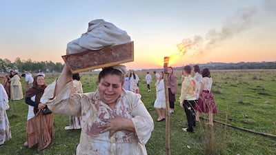 Una mujer angustiada sostiene un recipiente, rodeada de personas con antorchas en un ambiente dramático y colorido.