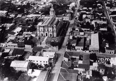 Edificio colonial con cúpula en el centro de una cuadrícula de calles y casas de un piso en un ambiente tranquilo.