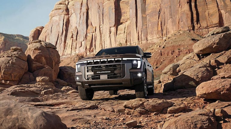 Camioneta Musso en primer plano sobre terreno pedregoso, rodeada de rocas y un paisaje árido.