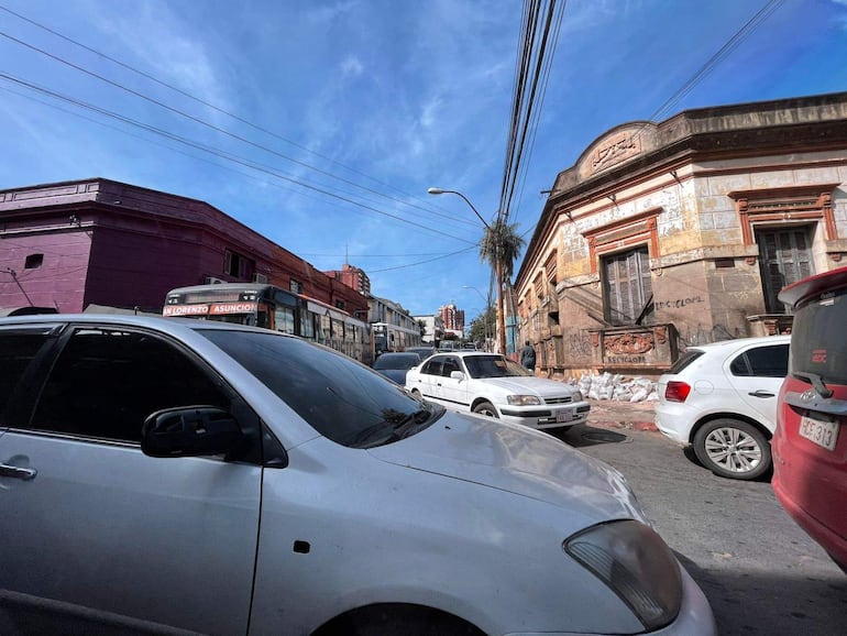 Escena urbana en Asunción con vehículos en movimiento y un autobús cerca de un edificio deteriorado.