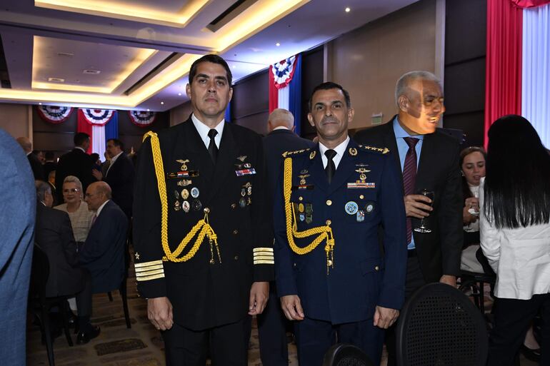 Oficiales en uniforme militar, uno de la Armada y otro de la Fuerza Aérea, en un evento decorado con los colores de la bandera paraguaya.