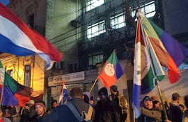 Grupo de campesinos con banderas en Asunción, algunos hablan y escuchan atentamente, mostrando emociones de tranquilidad y felicidad.