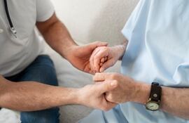 Imagen alusiva al Parkinson. Una persona toma las manos de otra que lleva una bata de hospital.