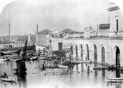 Embarcaciones en el puerto de Asunción rodeadas de agua debido a inundaciones, con edificios de estilo clásico al fondo.