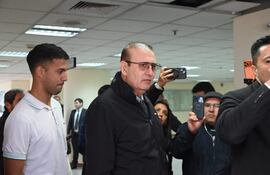 Erico Galeano Segovia con chaqueta oscura y lentes, junto a joven serio en camiseta blanca, rodeados de personas en un evento interno.