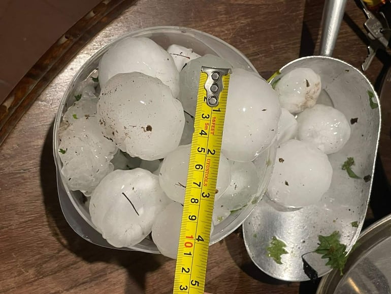 Bolas de granizo en recipiente, junto a regla amarilla que indica tamaño, en una mesa de madera.