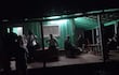 Grupo de personas conversando en un entorno oscuro y acogedor, con luz verde tenue en el techo.