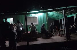 Grupo de personas conversando en un entorno oscuro y acogedor, con luz verde tenue en el techo.