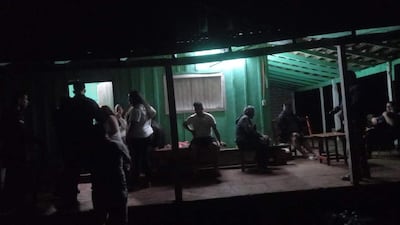 Grupo de personas conversando en un entorno oscuro y acogedor, con luz verde tenue en el techo.