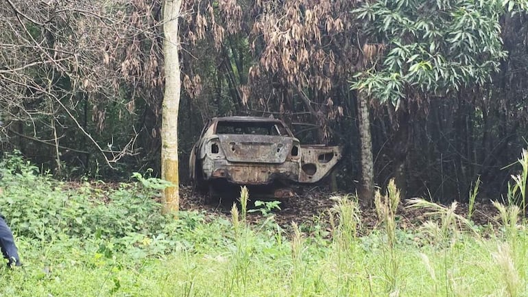 Camioneta abandonada y quemada en entorno natural, rodeada de vegetación y árboles secos, sin personas visibles.