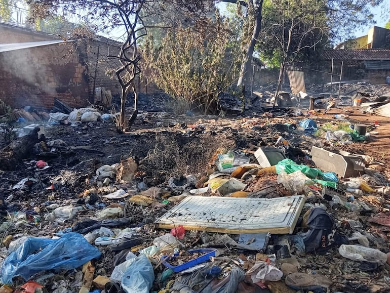 Terreno desolado con basura y escombros, sin personas visibles ni estructuras reconocibles, reflejando abandono tras incendio.