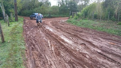 Ciclista con mochila avanza por camino de barro, mientras un auto atascado queda en el fondo rodeado de vegetación.