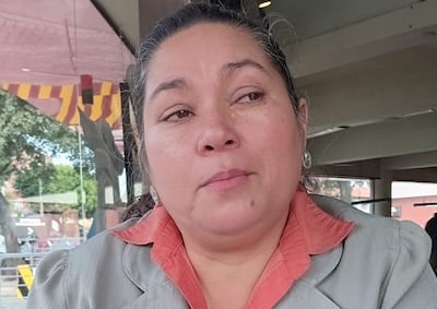 Clementina Ruiz Díaz Ojeda en chaqueta gris y blusa naranja, con expresión seria, sentada en un café, mirando hacia el exterior.