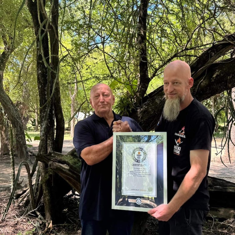 Wilbert Sawatzky sonríe mientras sostiene un certificado de Guinness y estrecha la mano de otro hombre en un entorno natural.