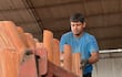 Hombre en camiseta azul y guantes oscuros organiza tejas terracota apiladas en un vehículo en un ambiente industrial.