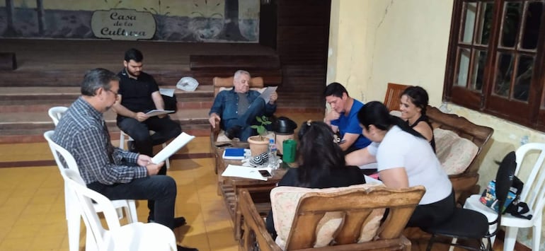 Grupo de seis personas en Casa de la Cultura, interactuando. Hombres y mujeres, algunos leyendo, en un entorno amistoso.