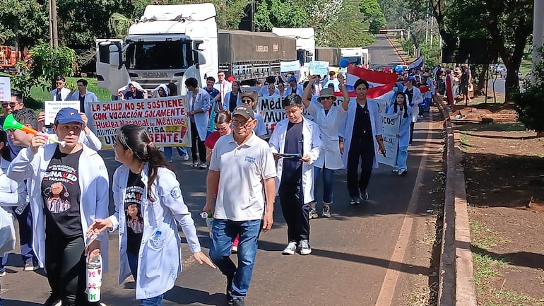 Grupo de médicos con batas blancas y pancartas en Ciudad del Este, algunos con bocinas, expresan su descontento.