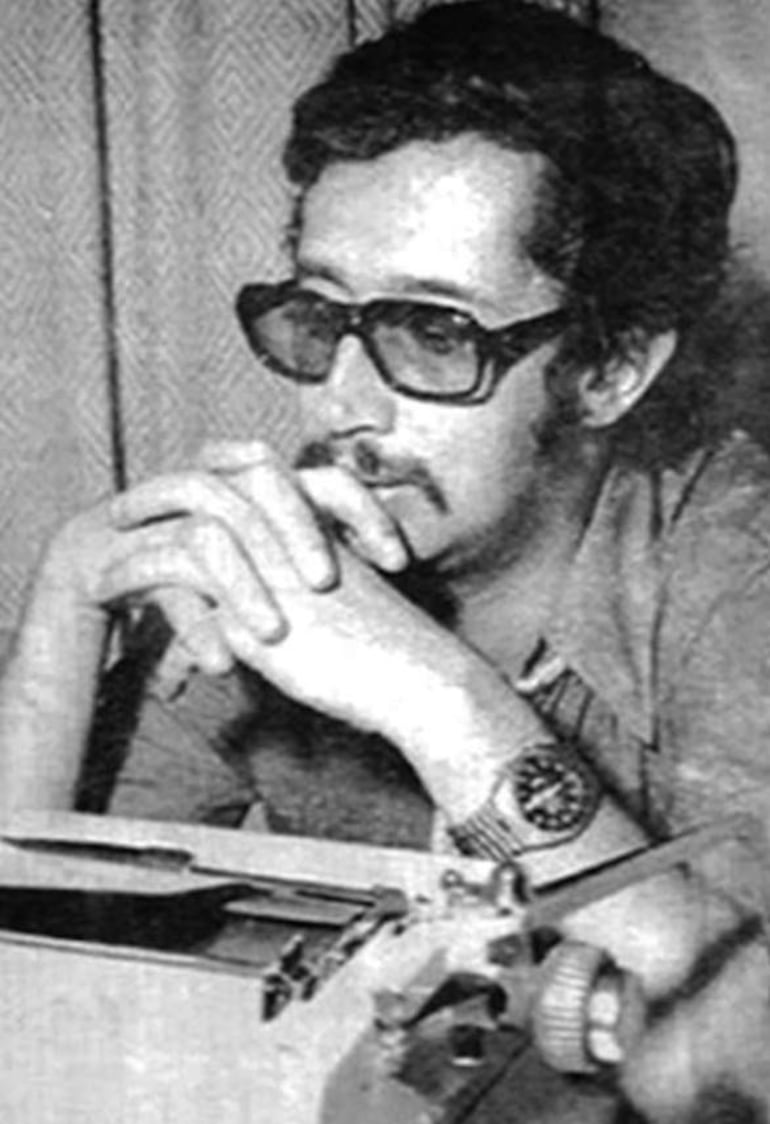 Galeano, con gafas oscuras y barba, mira pensativo su máquina de escribir en un ambiente tranquilo y acogedor.