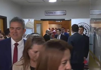 Carmen Dejesús Giménez de Ovando en chaqueta formal, rodeada de diputados en un pasillo del Congreso con carteles visibles.