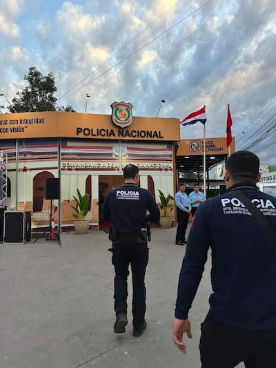 Dos policías en uniforme oscuro junto al edificio de la Policía Nacional, observando un entorno despejado y nublado.