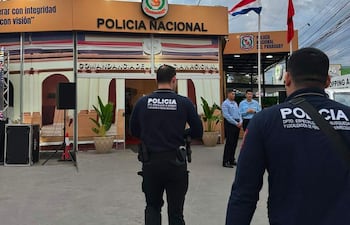 Dos policías en uniforme oscuro junto al edificio de la Policía Nacional, observando un entorno despejado y nublado.