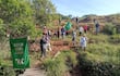 Grupo de productores con banderas verdes y cartel en mano, rodeados de vegetación y un camino de madera.