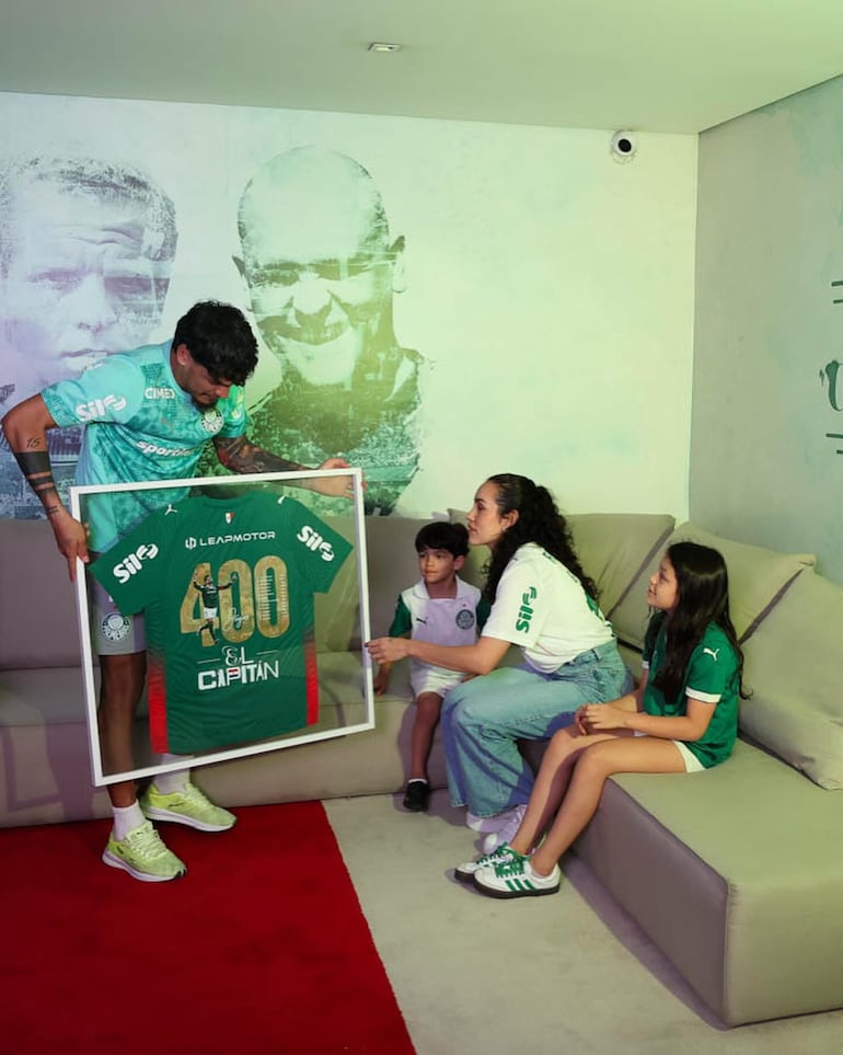 Gustavo Gómez mostrando el cuadro con la camiseta de los 400 partidos con el Palmeiras a su esposa Jazmín Torres y sus hijos Pía y Lucca. (Instagram/Gustavo Gómez)