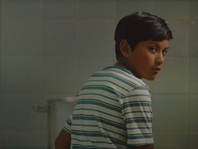 Niño con cabello corto y camiseta de rayas observa con curiosidad en un entorno de cocina con azulejos.