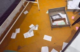 Consultorio desordenado con documentos esparcidos y una botella de plástico vacía en un suelo de baldosas amarillas.