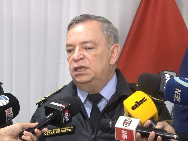 César Silguero en uniforme policial frente a micrófonos, rodeado de periodistas en un ambiente institucional.