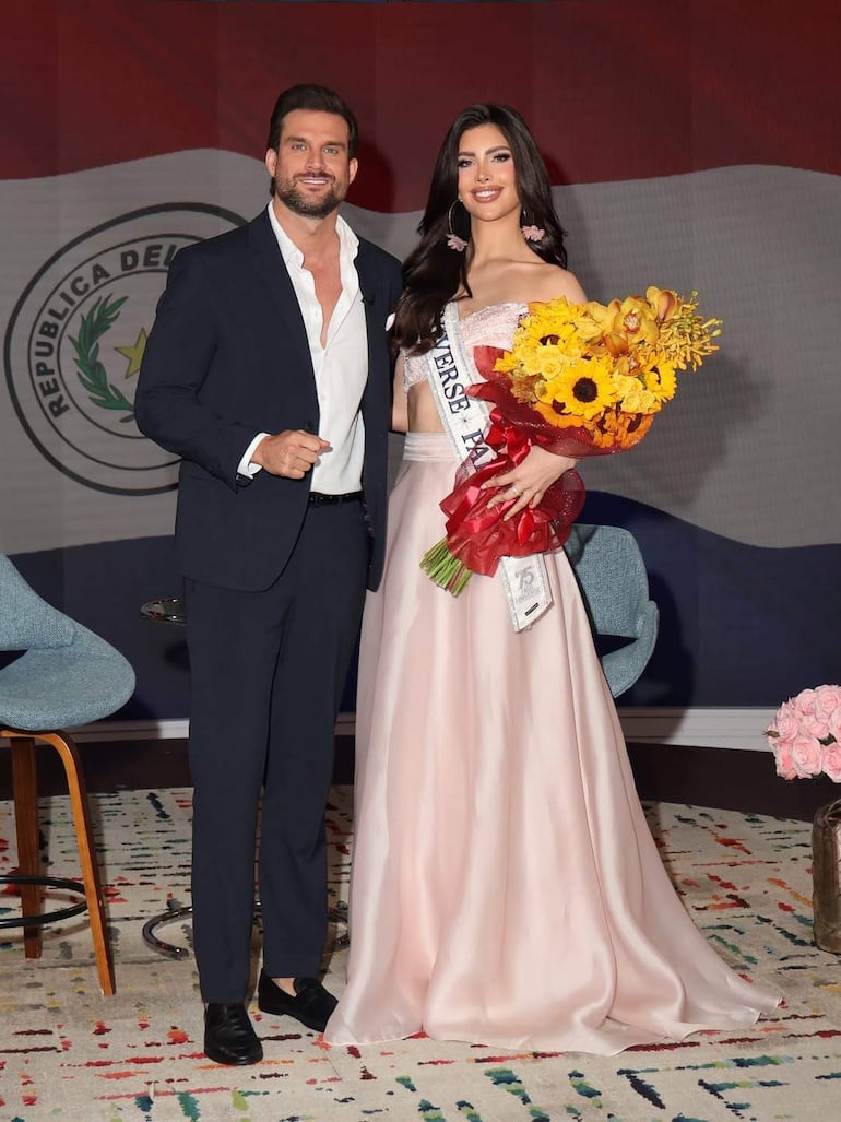 Gretha Matiauda sonriente en vestido rosa, junto a un hombre en traje oscuro, en un ambiente decorado con flores y bandera paraguaya.