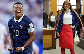 Mbappé en uniforme azul de Francia sonríe junto a mujer con blusa blanca y falda roja, en ambiente interior.