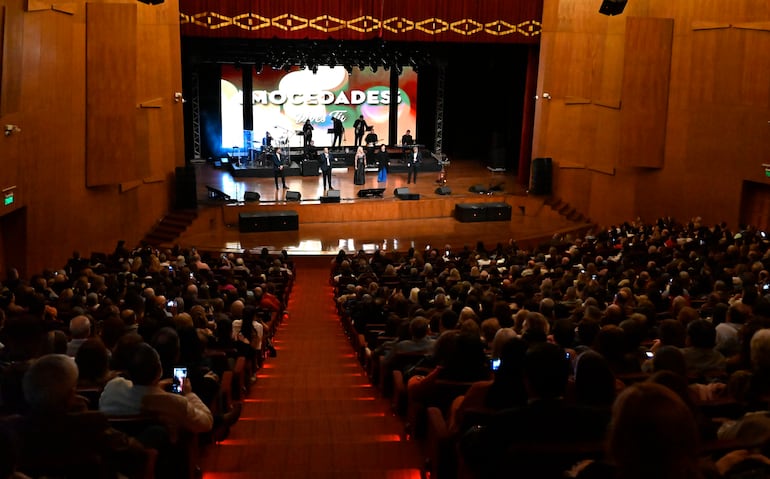 Músicos de Mocedades en el escenario, rodeados de un público entusiasta que sostiene teléfonos móviles.