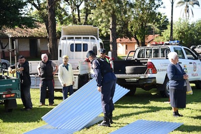 Hombre en uniforme policial agachado sobre chapas metálicas mientras otros observan. Ambiente tranquilo y árboles al fondo.