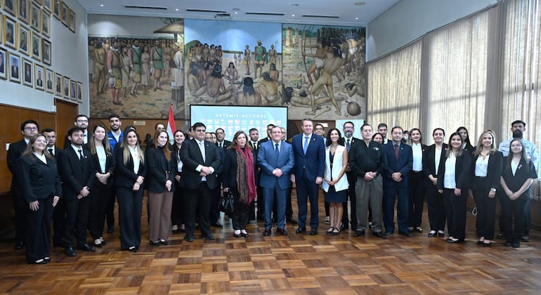 Grupo de personas en trajes oscuros en ceremonia formal, con Osvaldo Almirón Riveros al centro, abrigos y expresión de felicidad.