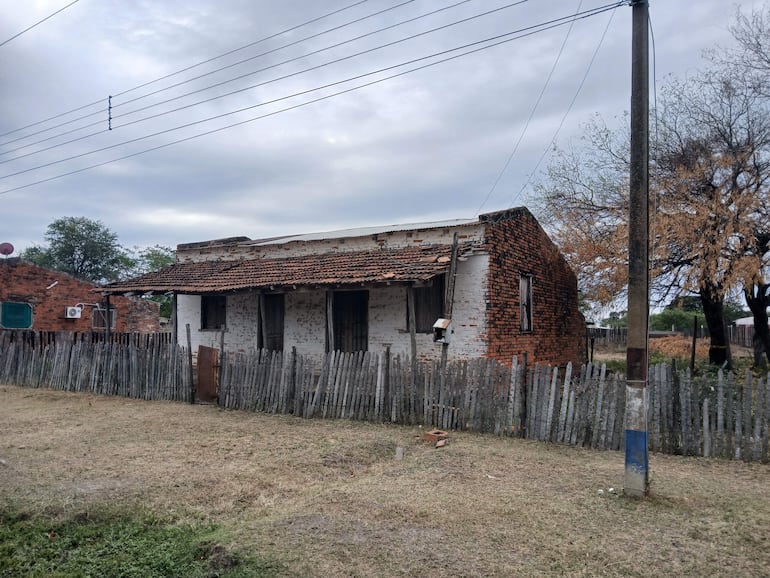 Casa deteriorada en un entorno rural, con techo de tejas faltantes y cerca en descomposición.