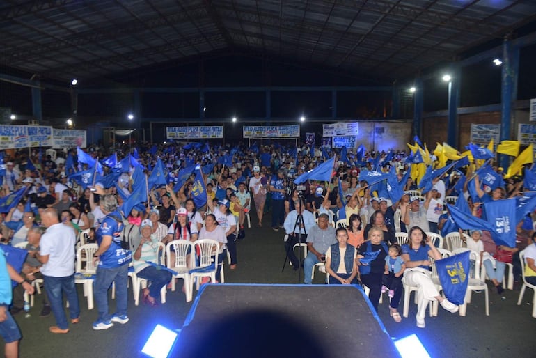 Multitud con banderas azules y amarillas, escuchando atentamente a María Portillo en un evento emocionante.
