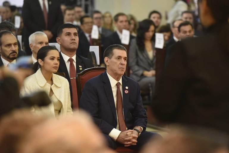 Horacio Cartes con traje oscuro y corbata burdeos, mientras Juan Manuel Nungaray escucha con atención a su lado en un entorno formal.