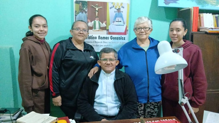Cuatro mujeres, sonrientes y vestidas con abrigo y chaquetas, rodean a un hombre en ropa clerical en un ambiente acogedor.