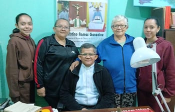 Cuatro mujeres, sonrientes y vestidas con abrigo y chaquetas, rodean a un hombre en ropa clerical en un ambiente acogedor.