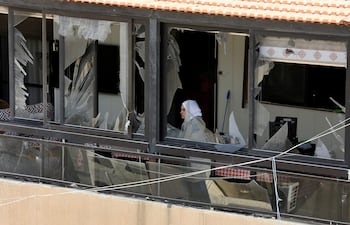 Una mujer observa tras las ventanas destrozadas de un edificio después un ataque aéreo israelí en la ciudad de Sidón.