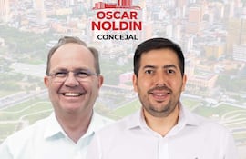 Camilo Pérez, con gafas y cabello gris, sonríe junto a Oscar Noldin, con barba y cabello oscuro, ante un fondo de ciudad.
