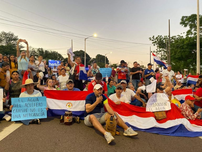 Hombres y mujeres en protestas, sentados y de pie, sosteniendo pancartas que defienden el acuífero Caacupé y el agua como recurso vital.