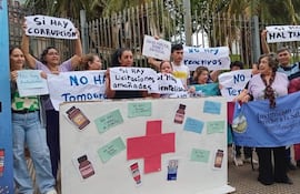 Un grupo de personas sostiene pancartas sobre salud pública, en un ambiente exterior con vegetación y una reja de fondo.