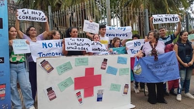 Un grupo de personas sostiene pancartas sobre salud pública, en un ambiente exterior con vegetación y una reja de fondo.