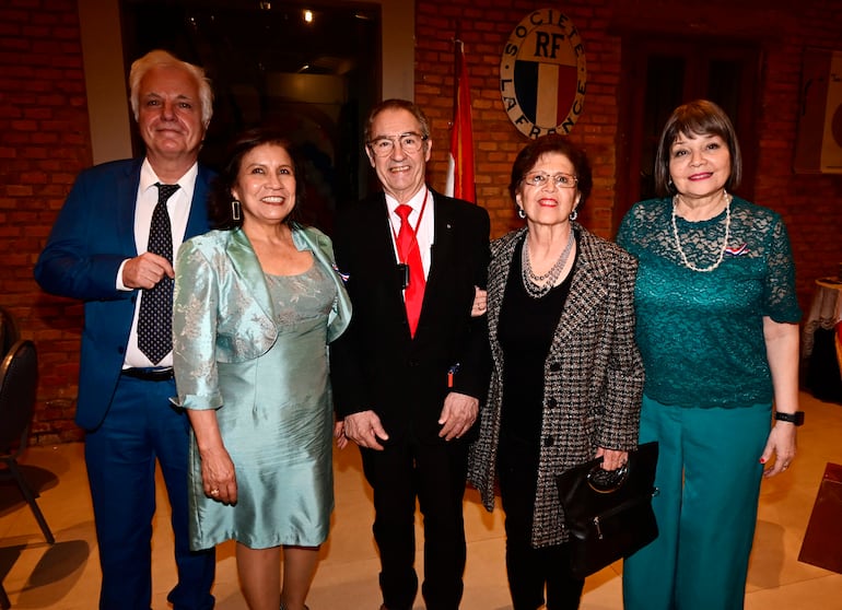 Cinco personas: hombre canoso en traje azul, mujer en vestido verde, otro hombre con saco negro y corbata roja, mujer con abrigo negro y otra en blusa azul.