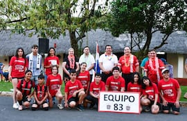 Grupo de quince personas con camisetas rojas que dicen 'PIONEROS', sonriendo y rodeados de un ambiente festivo al aire libre.